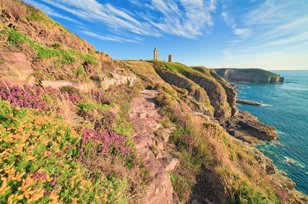 vue d'un phare breton au loin sur un sentier, venez découvrir les services de Trek Breiz